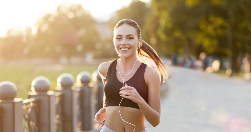 Cheerful woman with headphones running in park