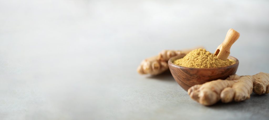 Ginger root and ginger powder in wooden bowl over grey concrete background with copy space. Immune