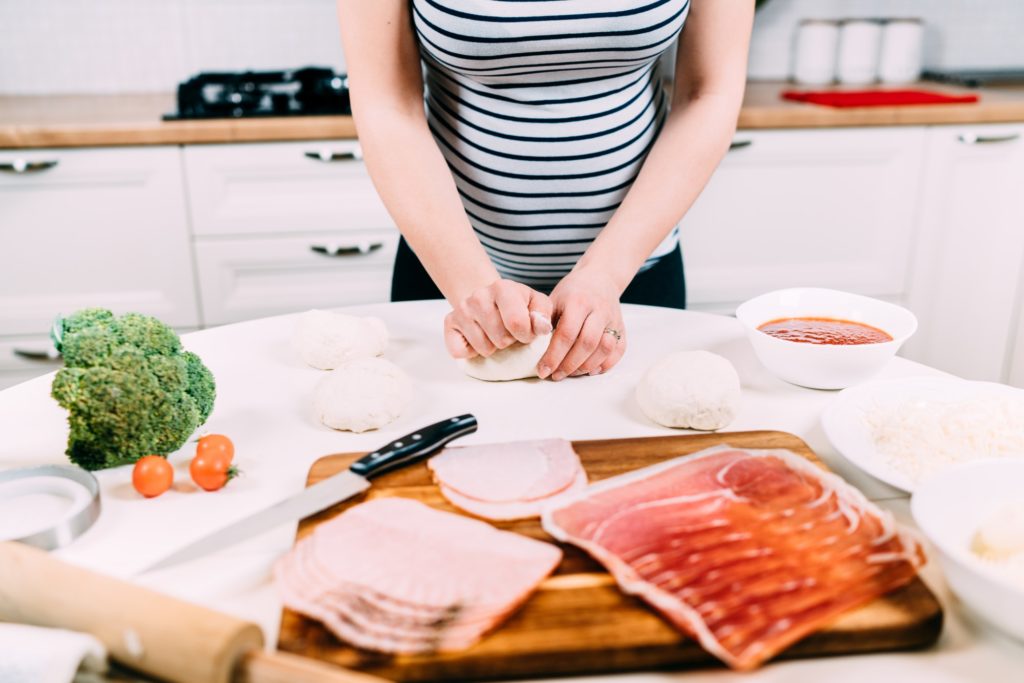 Pregnant woman cooking pizza and preparing dough