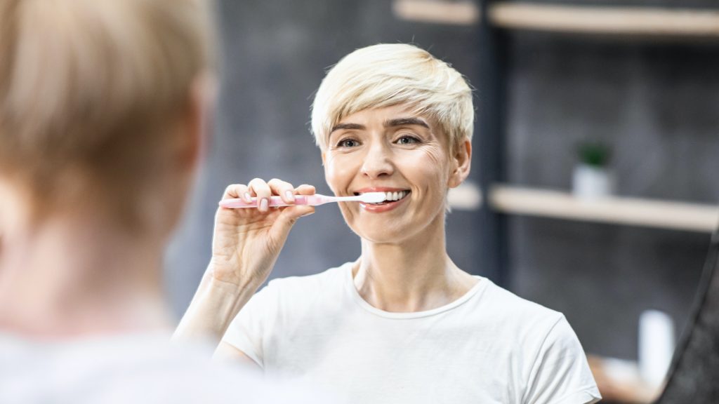 Woman avoiding cavities by brushing her teeth.