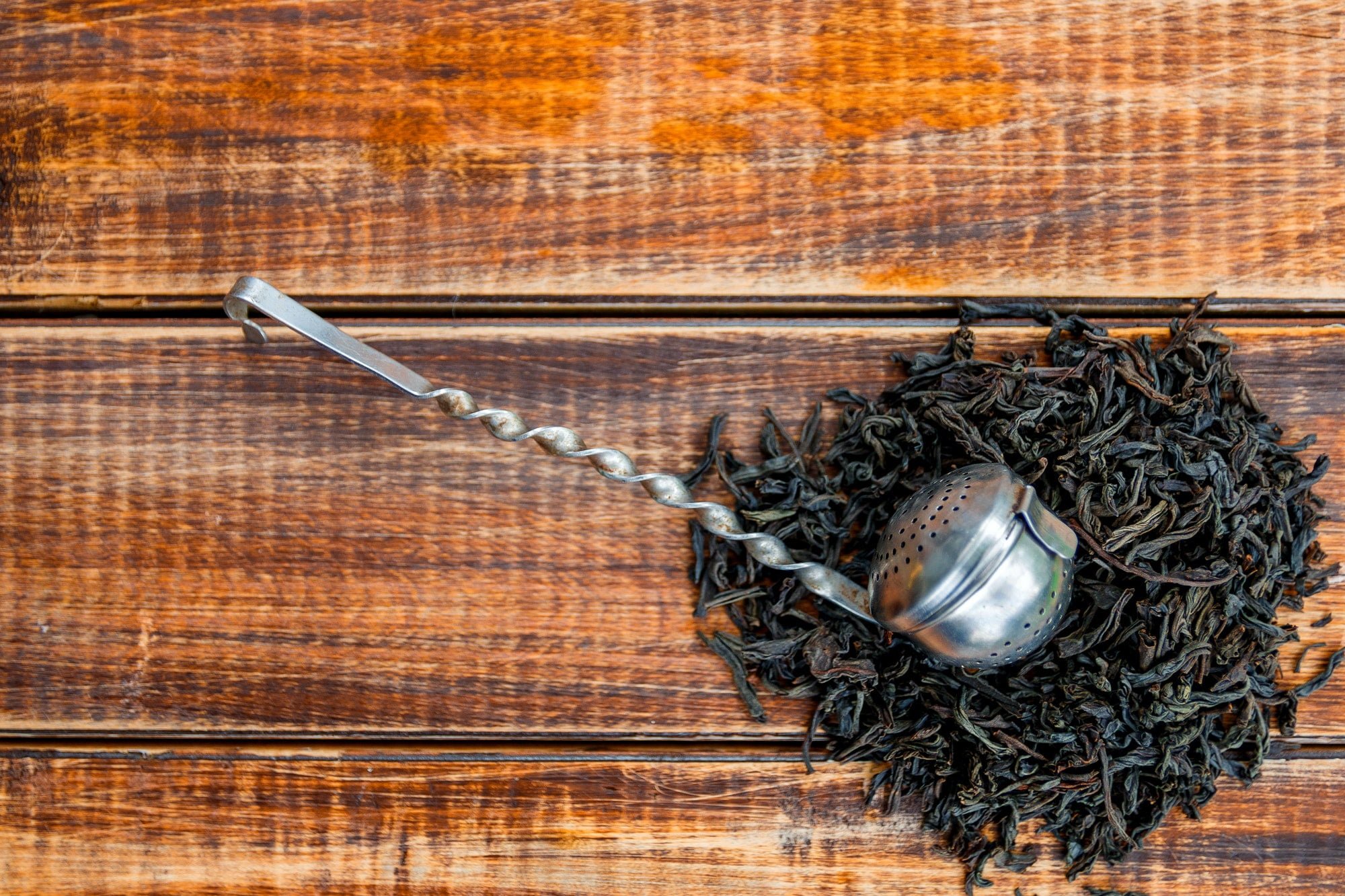 Vintage strainer with dry leaves of black tea on wooden