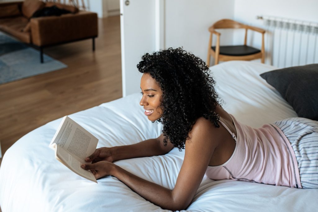 Woman lying down on bed reading a book