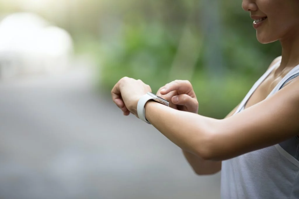 Woman runner looking at her smartwatch on park trail running tips for beginners.