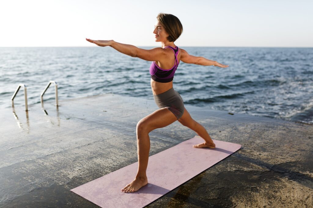 Young lady in sporty top and shorts practicing yoga with sea on background
