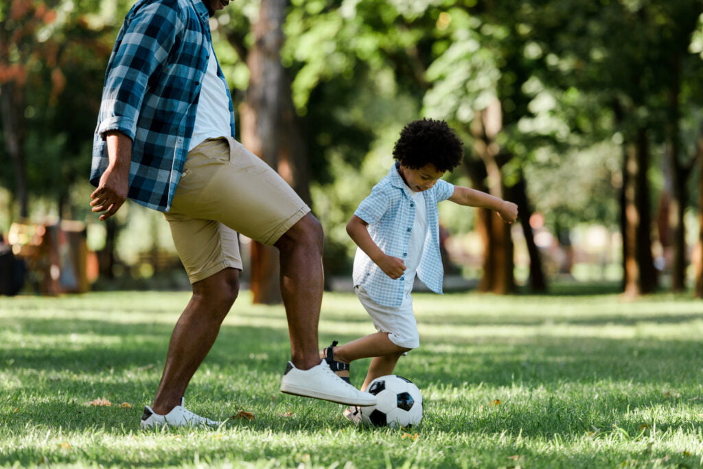 cropped view of african american father playing football with son - playing football soccer cures for boredom at home